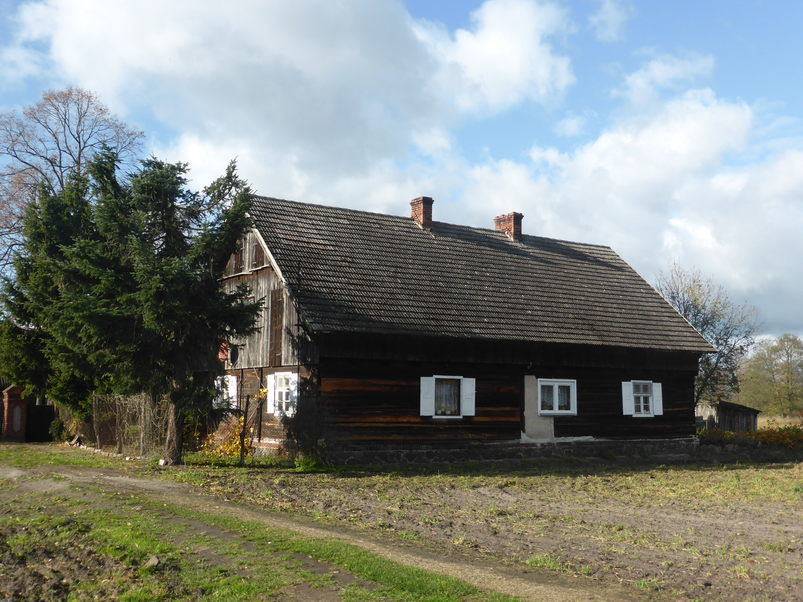 Stary parterowy dom z bali z dachem krytym dachówką, na niskiej kamiennej podmurówce, z deskowanym szczytem i białymi okiennicami